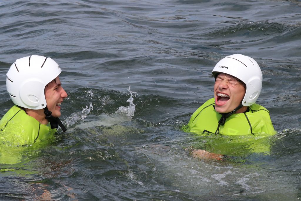 Twee lachende kampkinderen met helm in het water